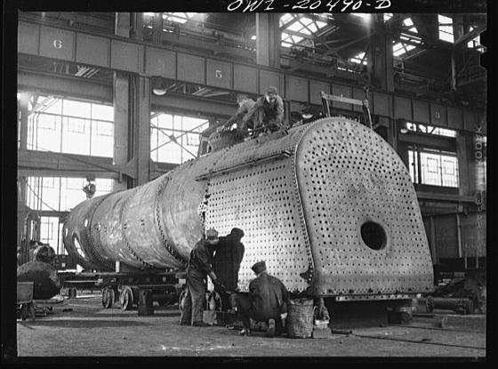 Old photo of a large industrial workshop with workers assembling a large train car.